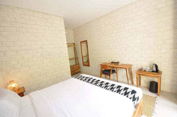 Cozy minimalist bedroom with white brick walls, wooden bed, desk, chair, and wardrobe.
